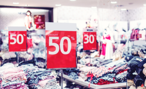 Tienda de ropa con carteles rojos que muestran precios competitivos con descuentos del 50% y 30% sobre las prendas.