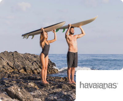 A man and a woman carrying surfboards on their heads while standing on a rocky shore, featuring a havaianas brand badge. This showcases Flipflow's ability to track brand visibility and competitive landscape in the lifestyle, footwear, and apparel industries.