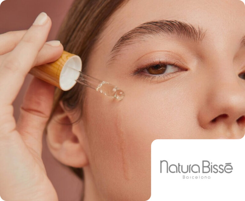 A close-up view of a person applying a skincare serum with a dropper directly to their cheek, featuring a Natura Bissé Barcelona brand badge. This demonstrates Flipflow's work in tracking product trends, pricing, and digital shelf performance in the luxury skincare and beauty market.