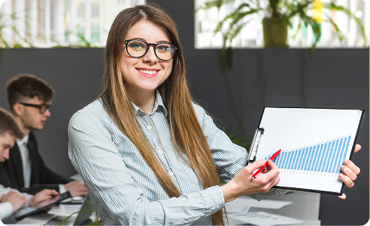 A smiling businesswoman wearing glasses presents an upward-trending bar graph on a clipboard to colleagues during an office meeting.