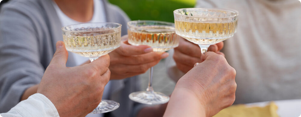 Close-up de várias pessoas brindando com taças estilo coupé, uma imagem social associada à exploração de sabores e ao ritual de consumo de gin.