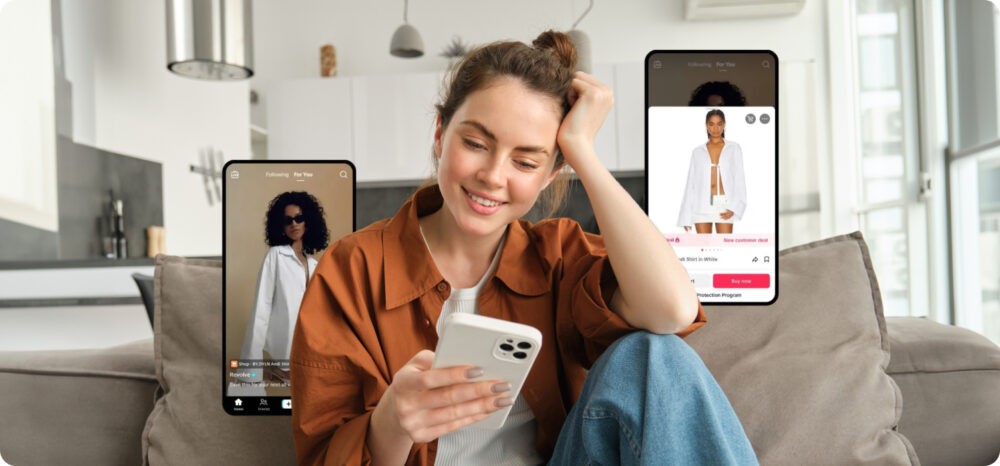 Una mujer joven sonríe mientras navega por TikTok Shop desde su teléfono móvil, visualizando artículos de moda en la aplicación. La imagen representa la comodidad de las compras sociales ante su expansión en Europa y el acceso a un mercado paneuropeo de tendencias.